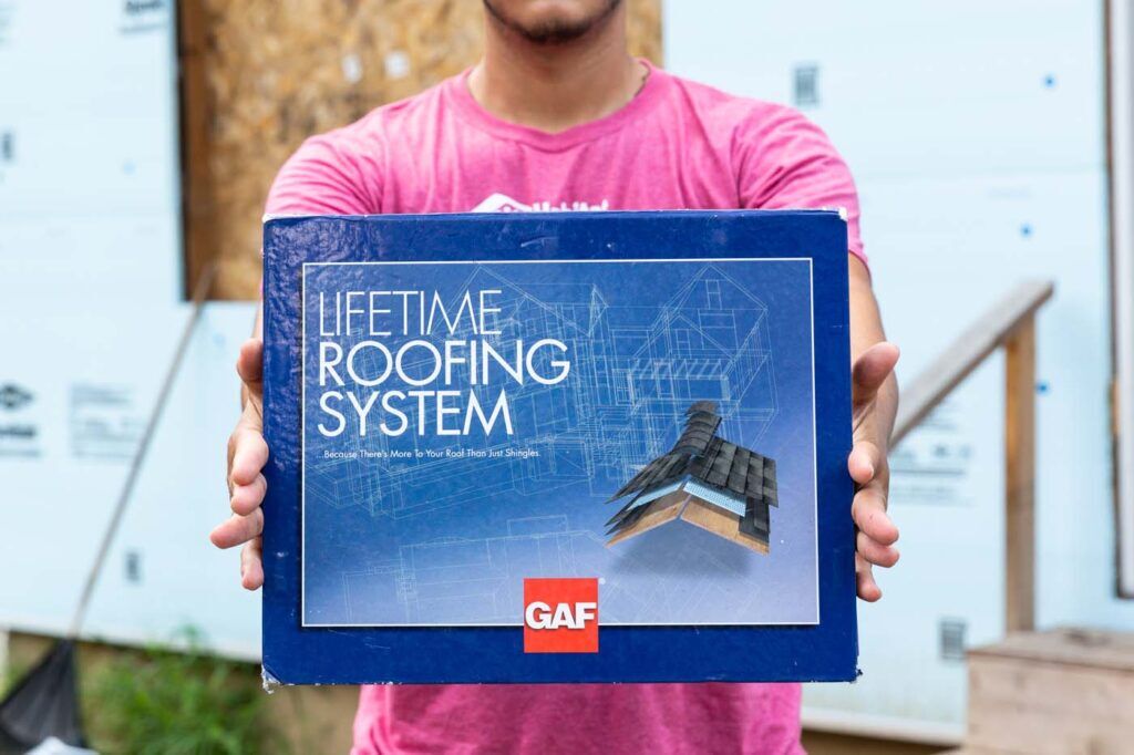 Person holding Lifetime Roofing System GAF certification. How To Find a Roof Warranty that Guarantees Protection.