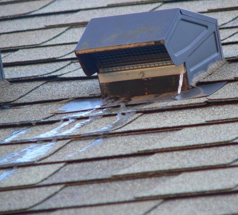 Leaking bathroom vent on roof with frozen water dripping from vent onto the roofs shingles