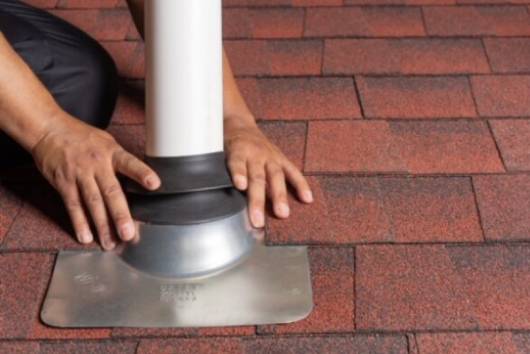 A person installing a vent on a roof on top of shingles