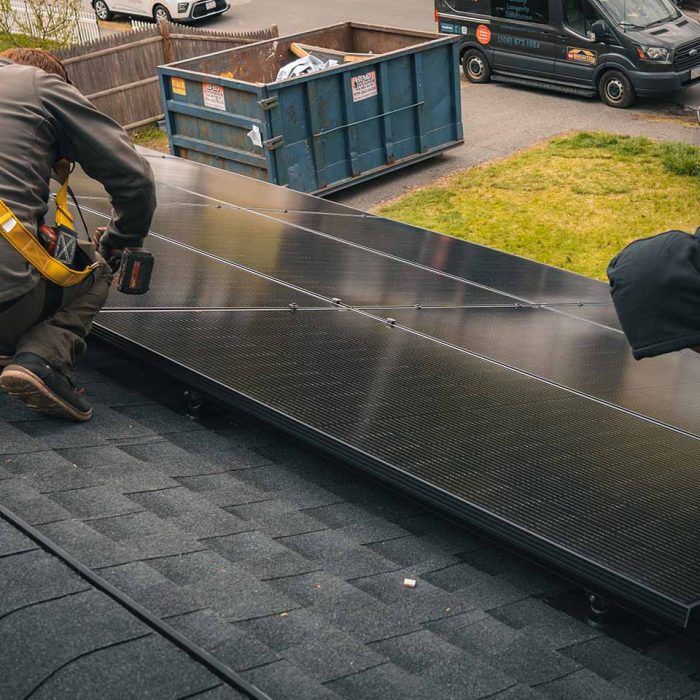 Two golden group roofers on a shingled roof installing solar panels on roof