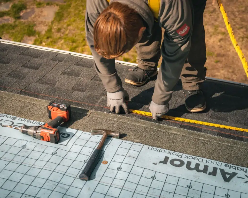 Golden Group roofer on a roof with safety equipment measuring and cutting shingles with a measuring tape