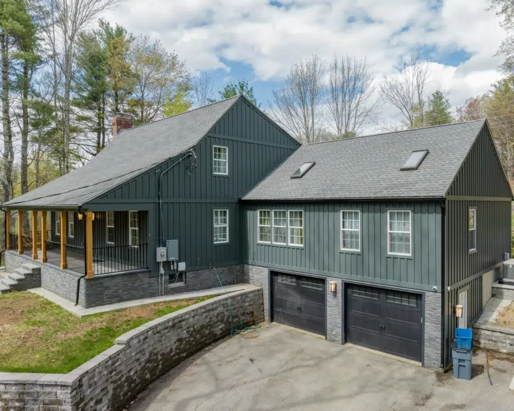 Exterior view of a large home with a two car garage and front porch with new midnight green siding on a slanted roof