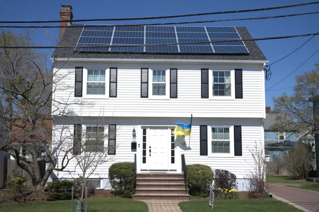 Street view of a residential home in Wayland, MA with white siding and newly installed solar panels on a shingled slanted roof