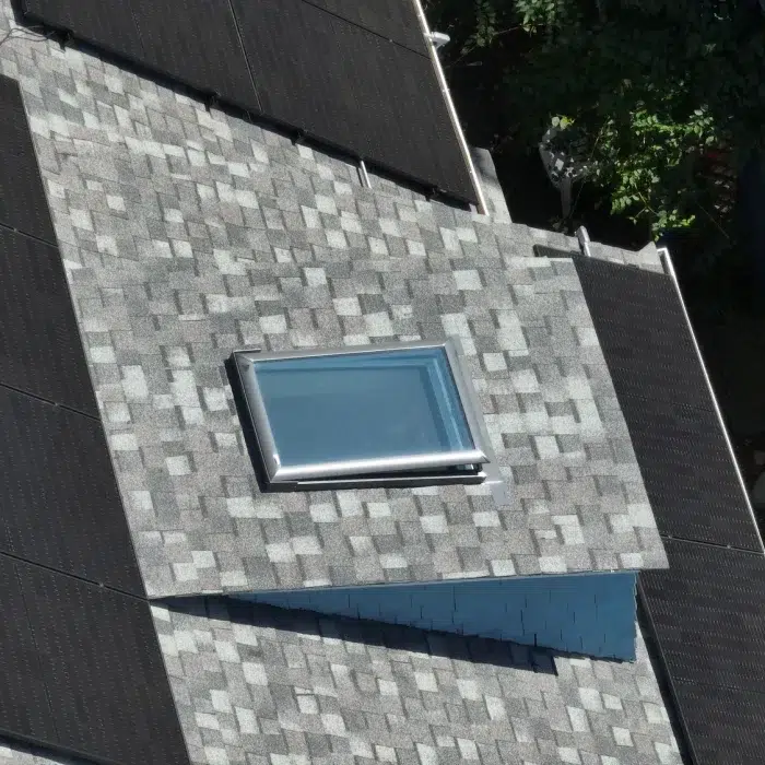 Multiple rooftop solar panels on a slanted shingled roof with a skylight in Newton, Massachusetts