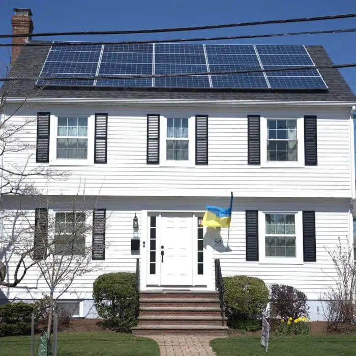 Street view of a residential home in Wayland, MA with white siding and newly installed solar panels on a shingled slanted roof
