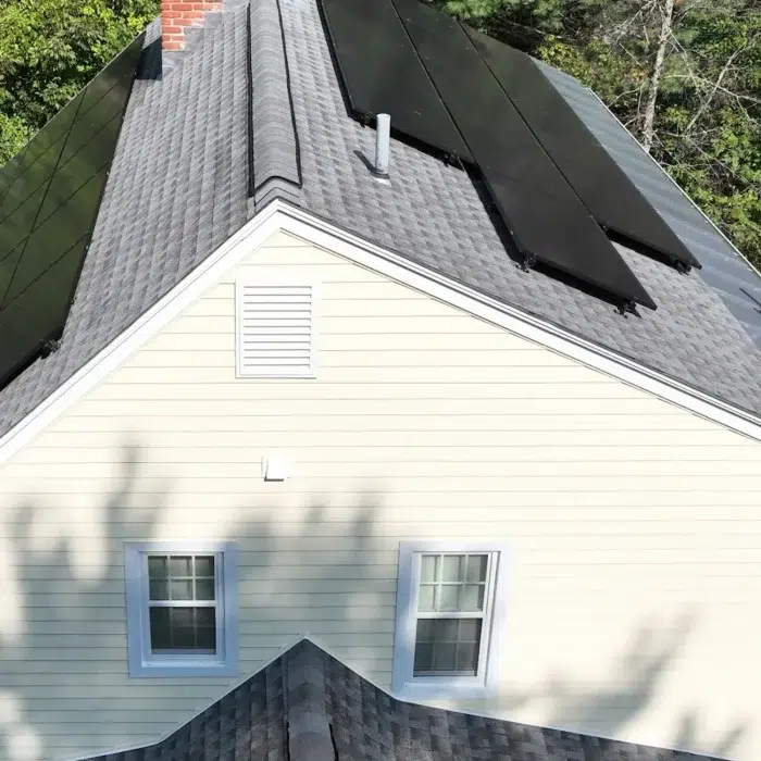 Solar panels on a slanted shingled residential roof surrounded by trees in Framingham, MA
