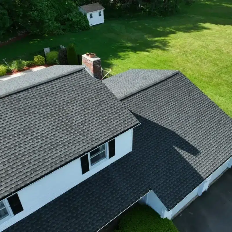 Aerial view of a new shingled Roof in Lexington, MA surrounded by green grass and bushes.