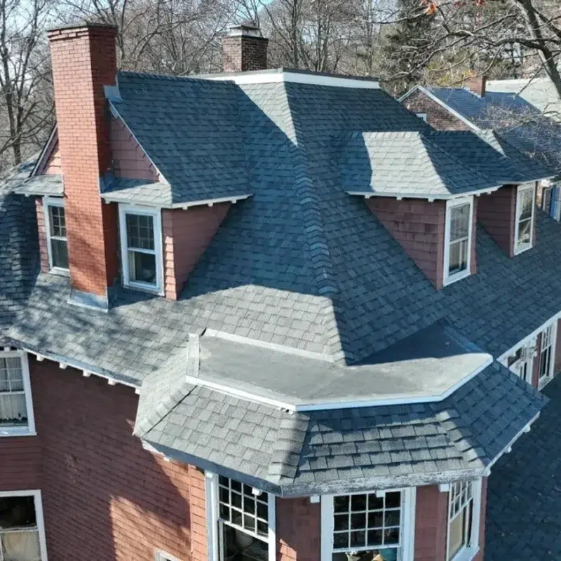 Aerial view of a large residential home with numerous roof tops with new shingles in Needham, MA by the Golden Group Roofing.